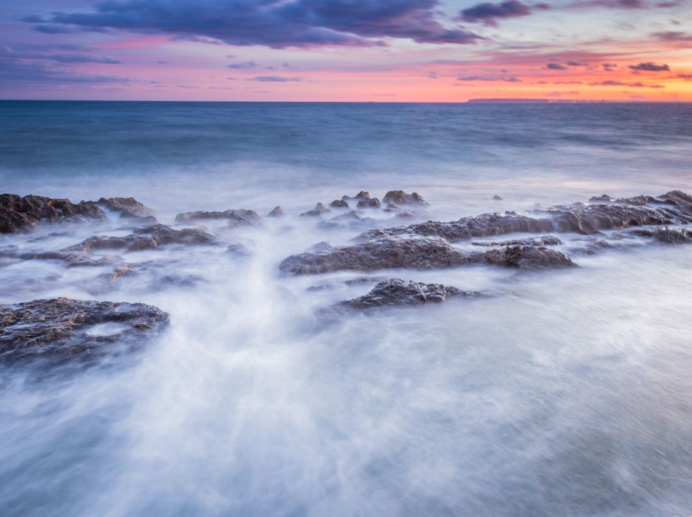 Sea waving near rough rocks during sunset