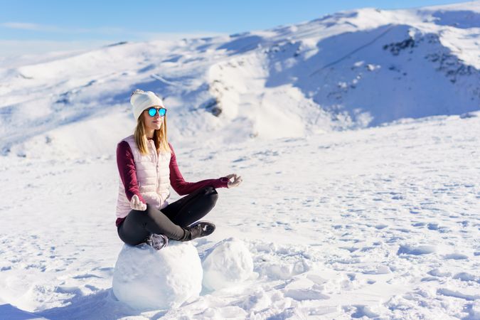 Woman in snowsuit meditating on snowy mountain