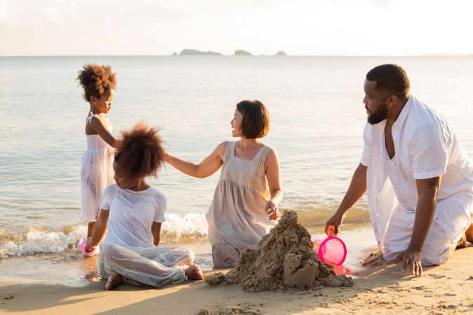 Black father and Asian mother playing in the sand with their children