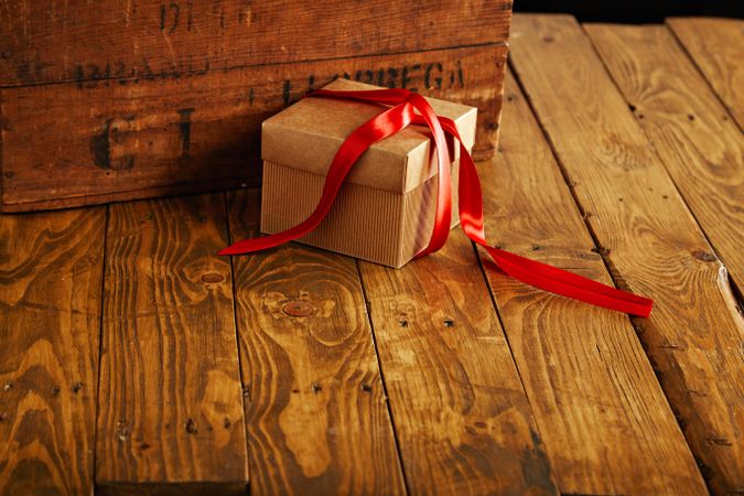 Cardboard box with red ribbon on wooden table