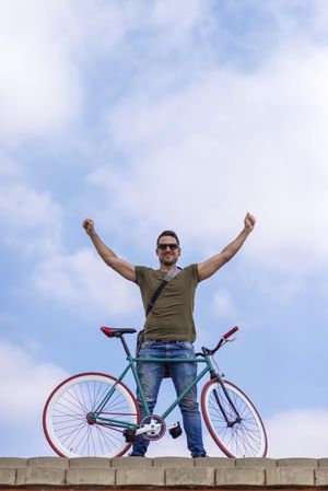 Male standing atop a roof with bike and arms up