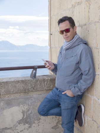 Man wearing sunglasses standing on a terrace while using his smartphone