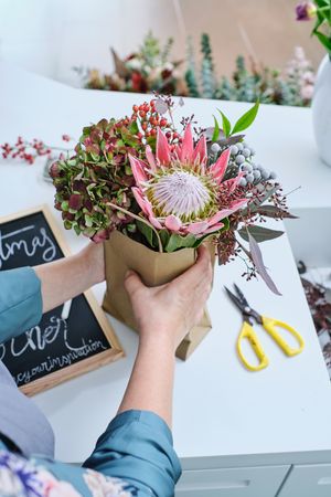 Crop female florist putting bouquet into paper bag