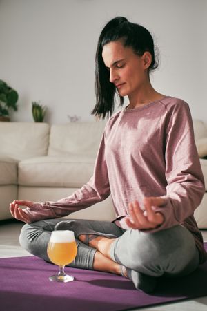 Woman meditating in Padmasana near glass of beer