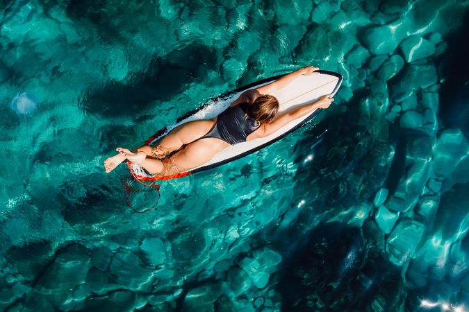 Aerial view with surfer woman on surfboard in transparent turquoise ocean