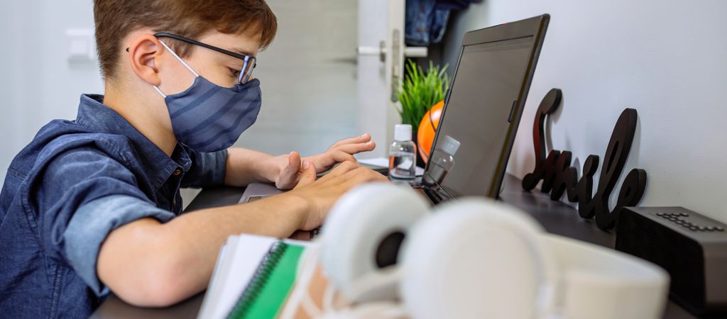 Teenager with face mask doing homework with laptop
