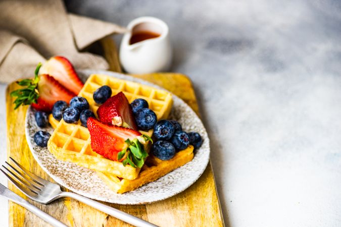 Waffle breakfast with blueberries & strawberries served with syrup on the side with copy space