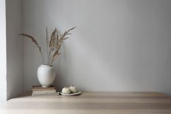 Elegant moody Scandinavian interior with dry grass bouquet in vase resting on old books next to mini pumpkins