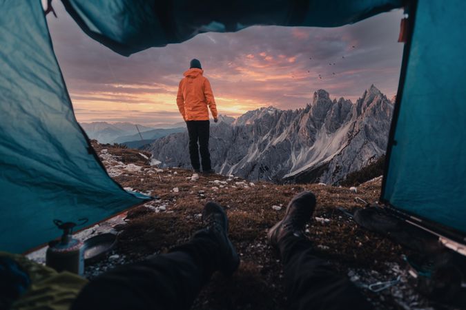 Cropped image of person in a tent looking at a person in orange jacket near mountainous landform