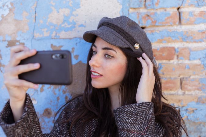 Charming Hispanic lady taking selfie near wall
