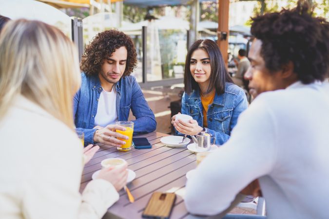 Multi-ethnic group of friends meeting up over coffee and juice at outside table