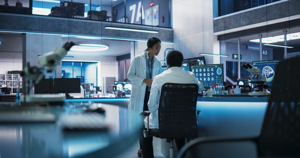 Medical Research Center In Modern Hospital: Female Asian Neuroscientist Talking To Black Male Doctor About CT Scans Of Human Brain.
