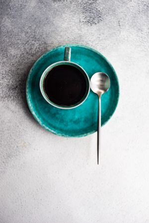 Top view of coffee cup on teal plate on marble table