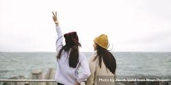 Woman in sweater holding up peace sign by sea with friend bGNPV4