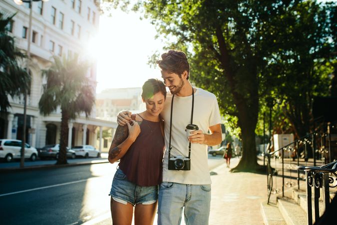 Happy explorer couple walking in the street holding a coffee cup with sun in the background