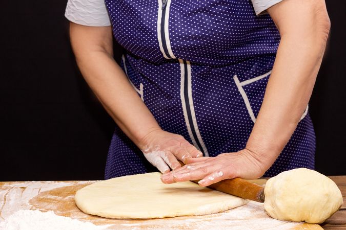 Cropped image of woman flattening a dough using rolling pin
