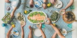 Group of people at blue patterned table with fresh fruits, salad, and vegetables wide composition