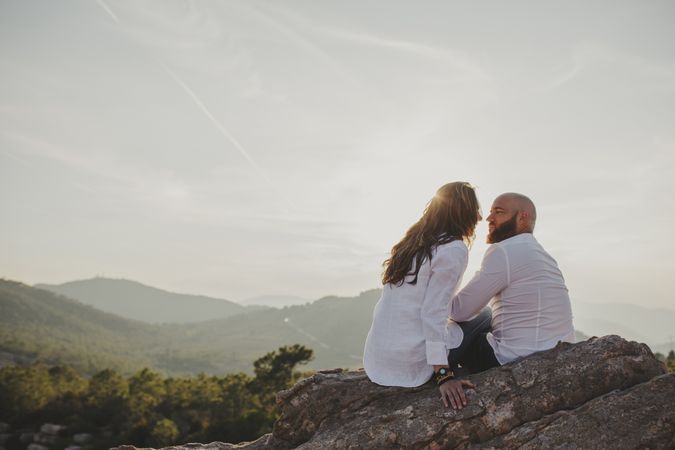 Happy couple sitting at mountain cliff
