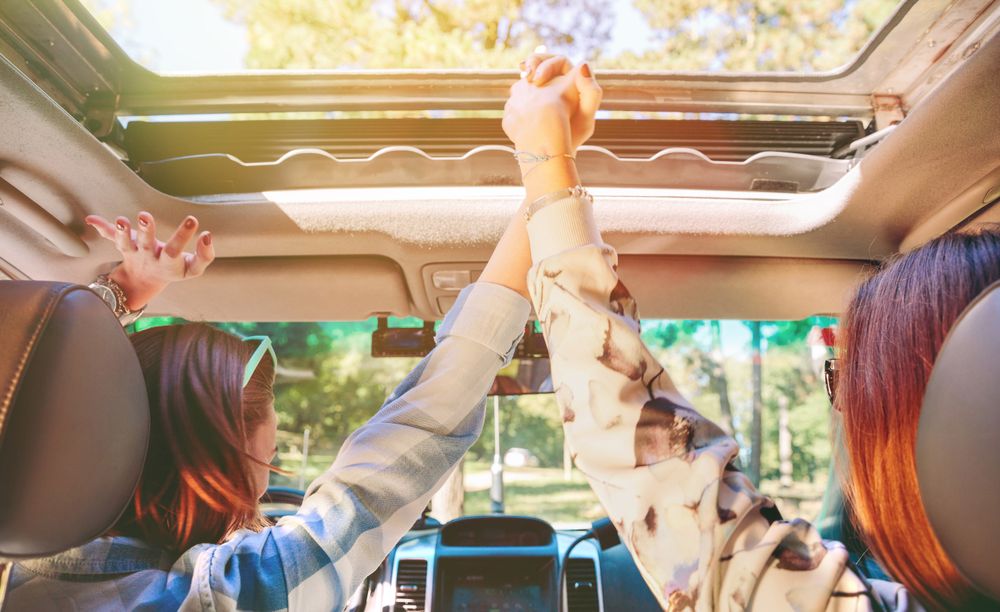 Happy women holding hands and raising arms inside of car