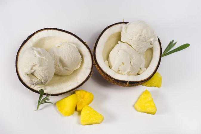 Top view of two coconut shells with ice cream and pineapple fruit chunks