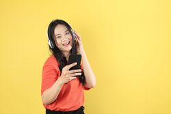 Young Asian Woman Listening to Music from Mobile Phone using Wireless Headphones