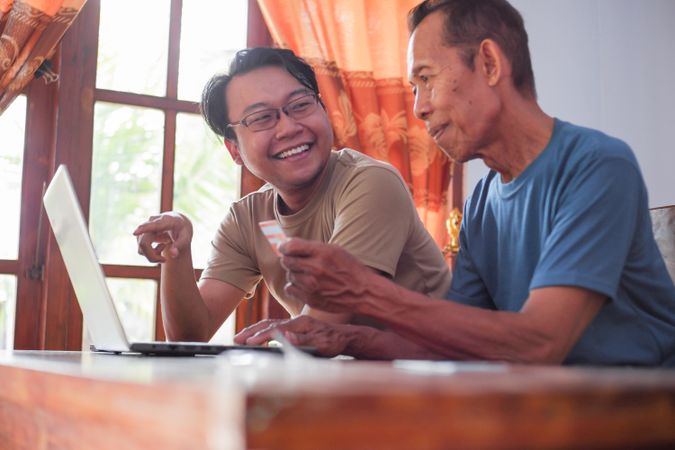 Happy adult son and mature father pay online using laptop and credit card