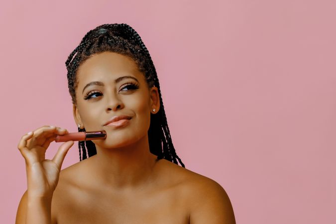 Curious Black woman holding lip gloss while looking up, copy space