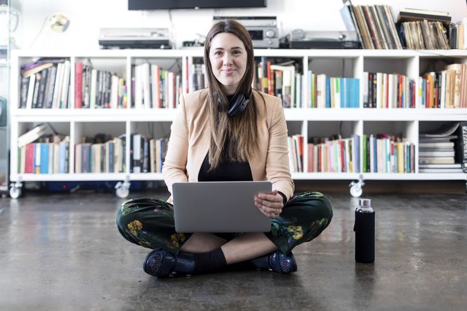 Portrait of a smiling woman sitting cross legged working on laptop with water bottle