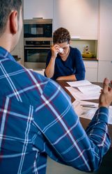 Woman holding tissue to face as her and her partner argue over bills