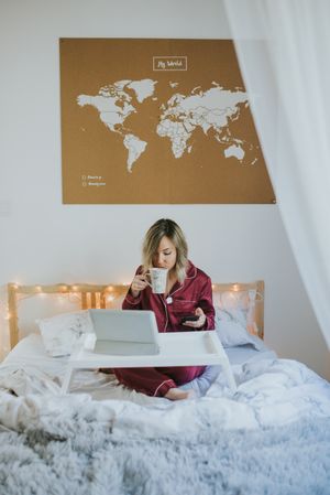Woman sitting in bed with tablet and looking on smartphone