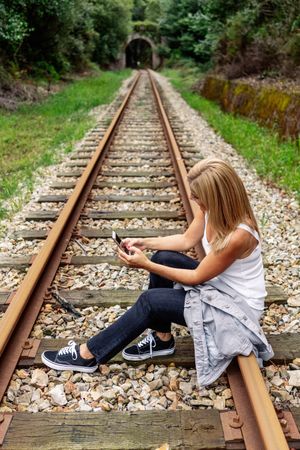Cheerful woman sitting on railway with smartphone