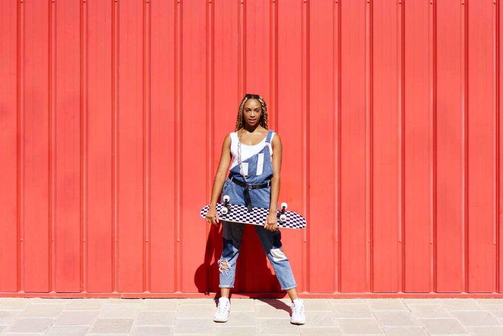Woman leaning against red wall with checkered skateboard