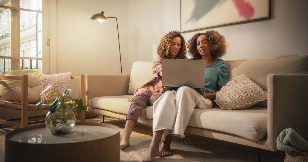 Portrait of Two Brazilian Young Women Using Laptop Computer While Sitting on a Sofa at Home.
