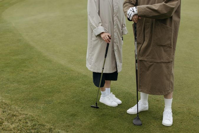 Two people in coats holding golf clubs