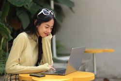 Happy Asian Girl Smiling and Working on Laptop Screen on Outdoor Coffee Shop