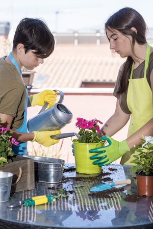 Two teenagers wearing a gardener apron watering plants on the terrace