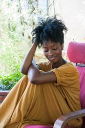 Young woman with curly bun and hoop earrings sitting in pink lounge chair looking down and smiling