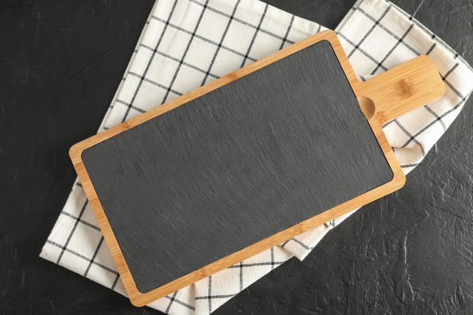 Cutting board with kitchen towel on dark background, top view