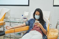 Woman in medical mask donating blood in clinic