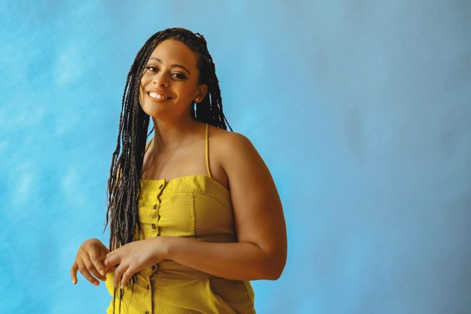 Shy female with long braided hair and hands across her torso in yellow one piece, copy space