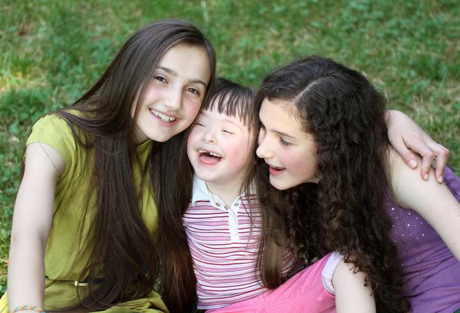 Three young women with their arms around each other sitting outside in the park