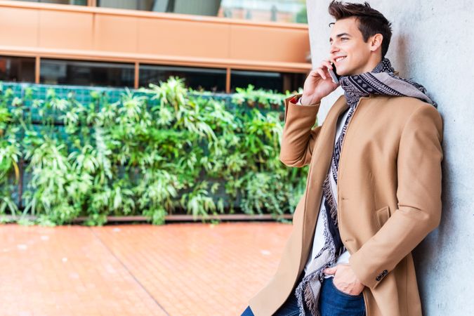 Smiling man in camel coat and scarf standing outside with phone to his ear