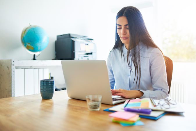 Woman in blue shirt working on her laptop in bright home office