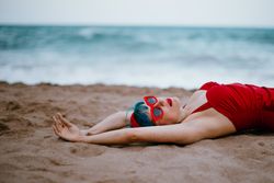 Relaxed woman in bright stylish swimsuit lying on sandy beach