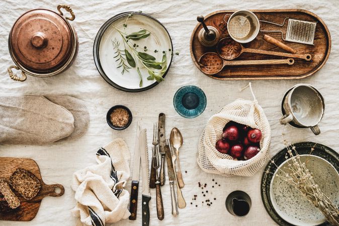 Vintage kitchen utensils artfully arranged on beige tablecloth, with onions, and bread
