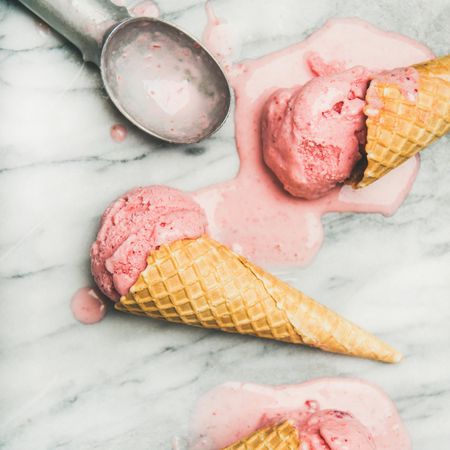Homemade strawberry yogurt ice cream in cones laying on marble counter top