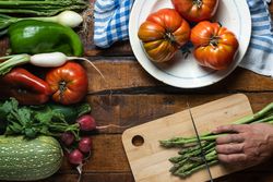 Cook cutting asparagus on table with mixed fresh vegetables