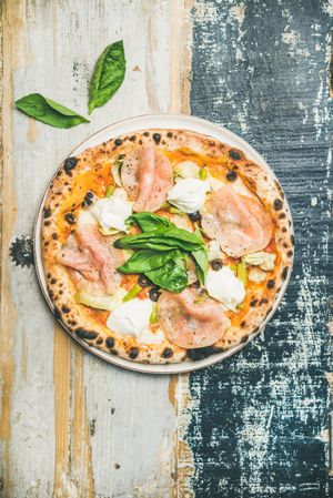 Freshly made wood fire oven pizza with spinach, ham and olives, on wooden background