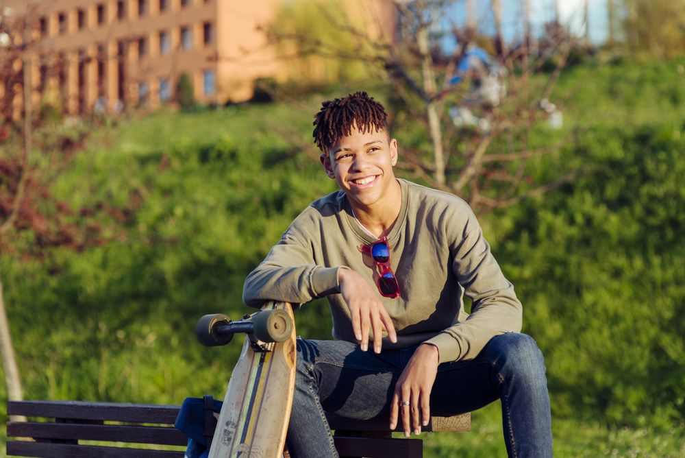 Young Black man sitting on bench with skateboard