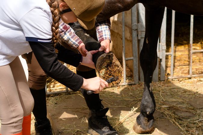 Girl cleans horse's hoof under supervision of instructor.